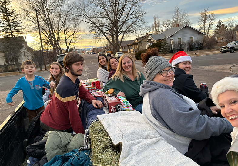 one child and six adults are on a flatbed trailer with hay for Christmas caroling