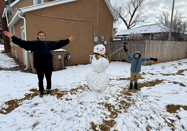 a dad and his son hold the branch-hands of the snowman they built.