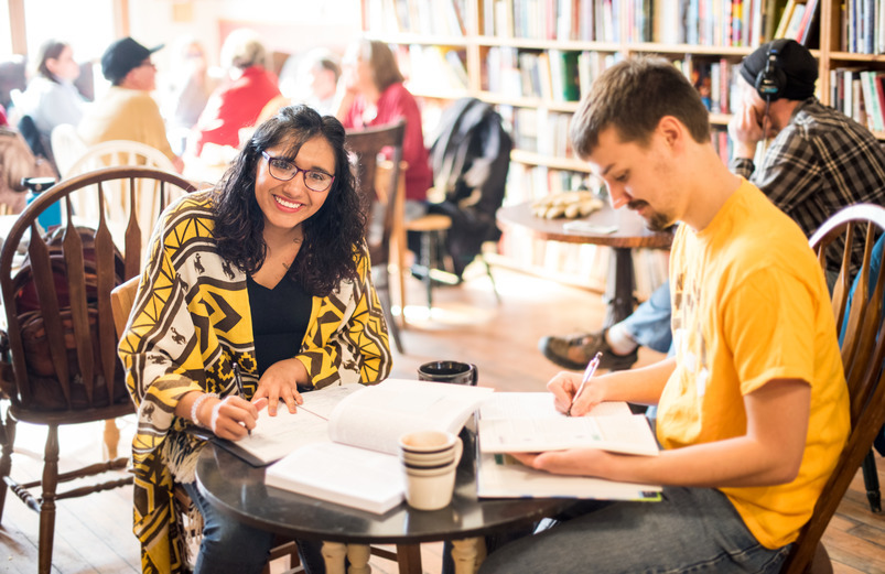 A man and a woman working at a table with a bookshelf in the background