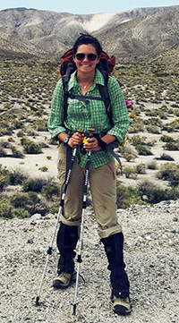 woman with treking poles and backpack standing in desert