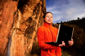  Assistant Professor Ye Zhang next to rock with laptop.