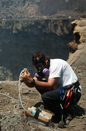 Scientist setting up research equipment on volcano wearing gas mask