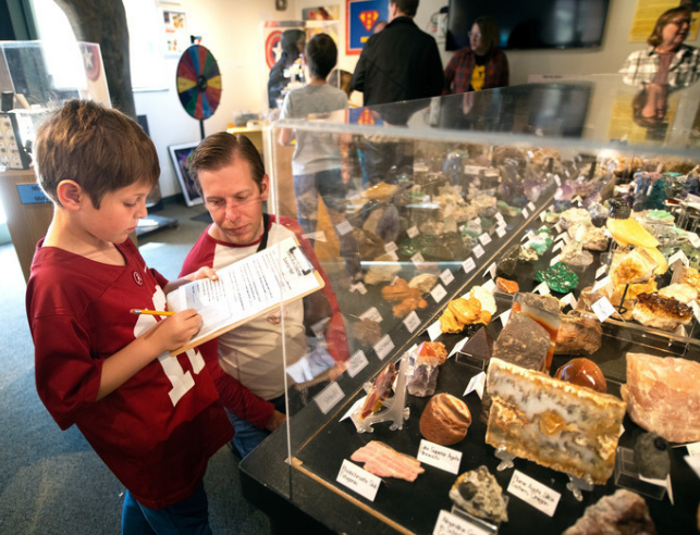 photo of child with adult filling out scavenger hunt in front of rock display case
