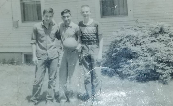 Three boys in an old photograph holding a basketball in front of a house