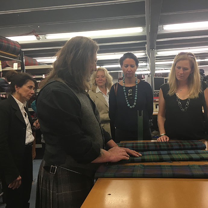 A group surrounds a man examining fabric for Scottish kilts.