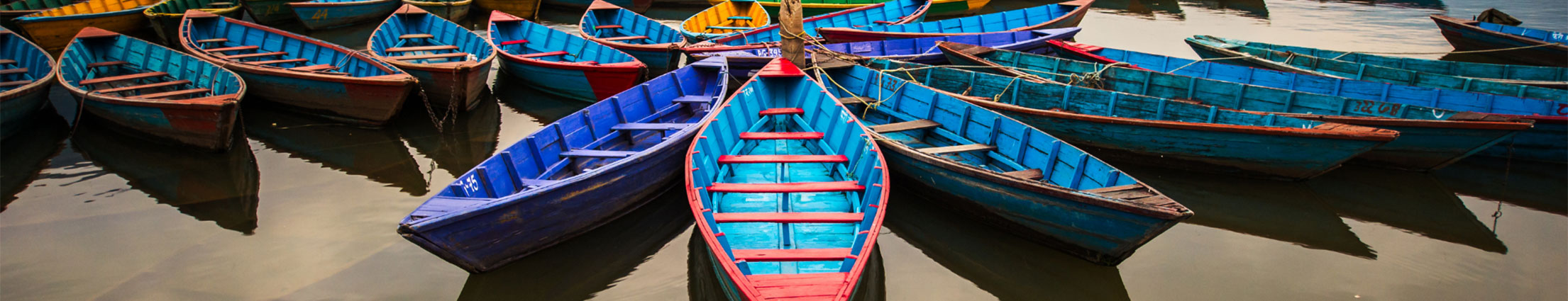 A line of blue and other multicolored boats sitting in water.