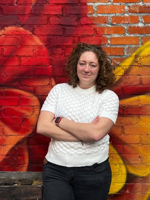 Erin Bentley smiling standing in front of a painted brick wall