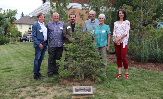 Rich Innes, William Gern, Michael Kern, Harold Bergman, Ann Boelter, and Diana Hulme pose for a group photo behind the tree and plaque dedicated to Bill Ruckelshaus.