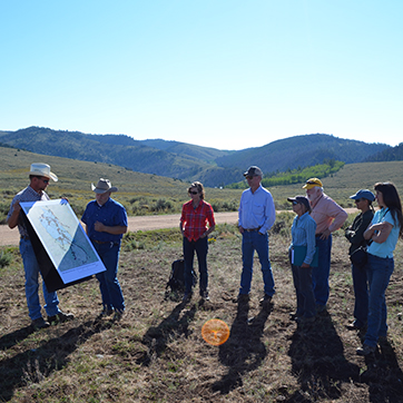 A group of people outside cluster around a man with a large map