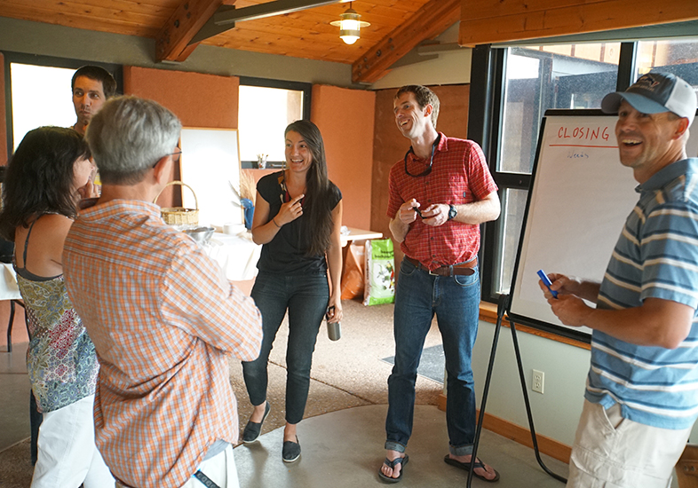 A group of people stand around a whiteboard on an easel, laughing