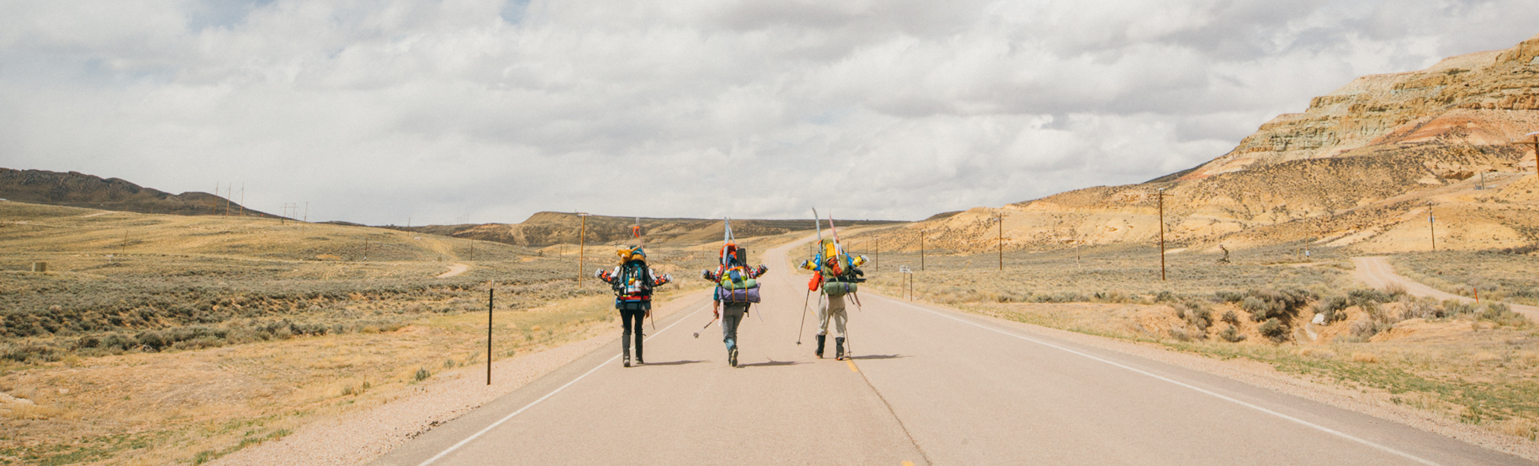 Three women with backpacks hike on a highway