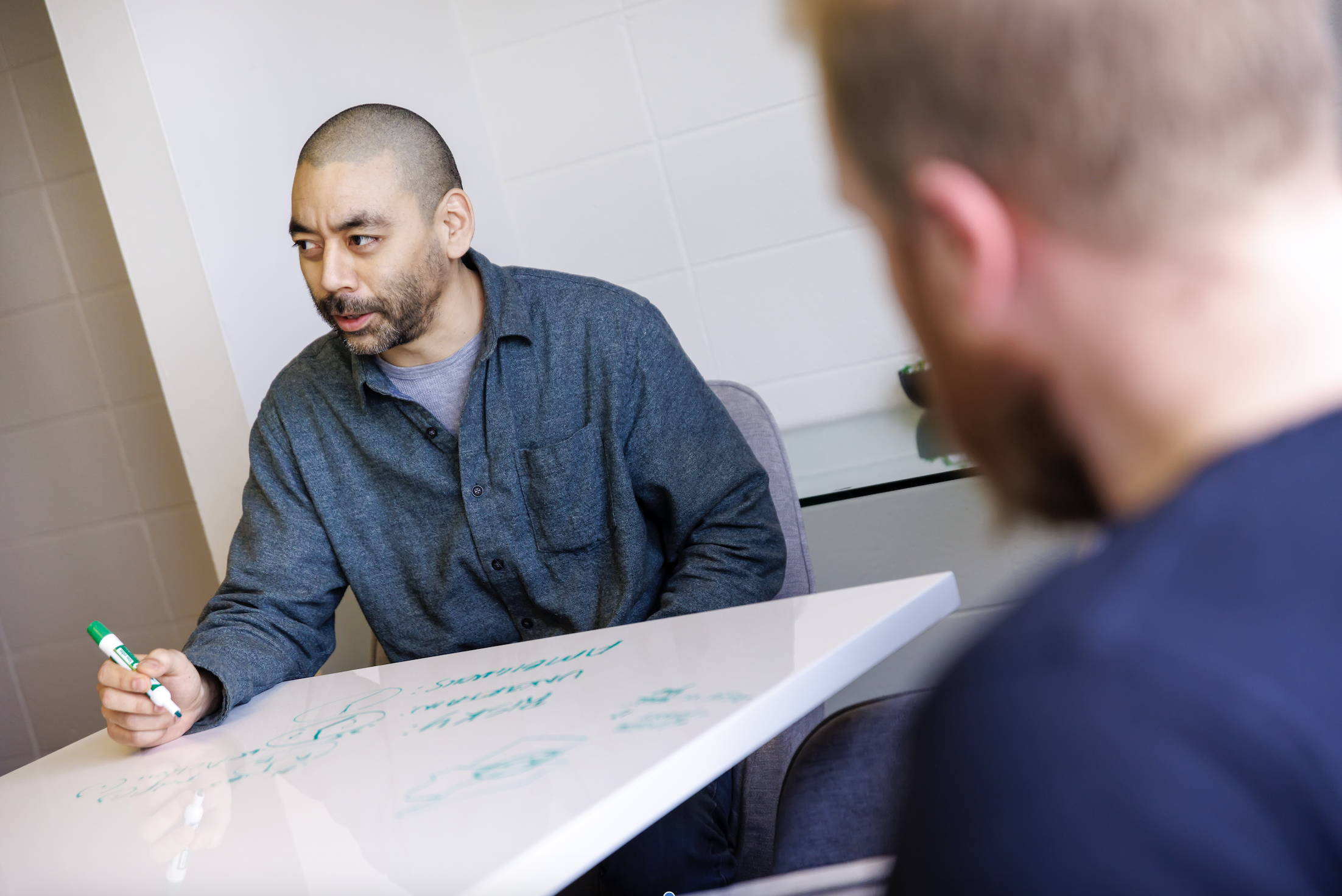 Person writing on a whiteboard table and discussing with coworkers