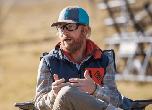Tom Grant sitting in a chair talking surrounding by grass landscape
