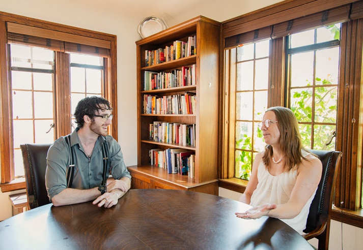 A student and advisor talk in the library room of the first floor of the Guthrie House with books lining the walls of the background.