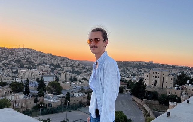 Andrew Bishop posing in front of a densely populated housing area with a setting sun light in the background.