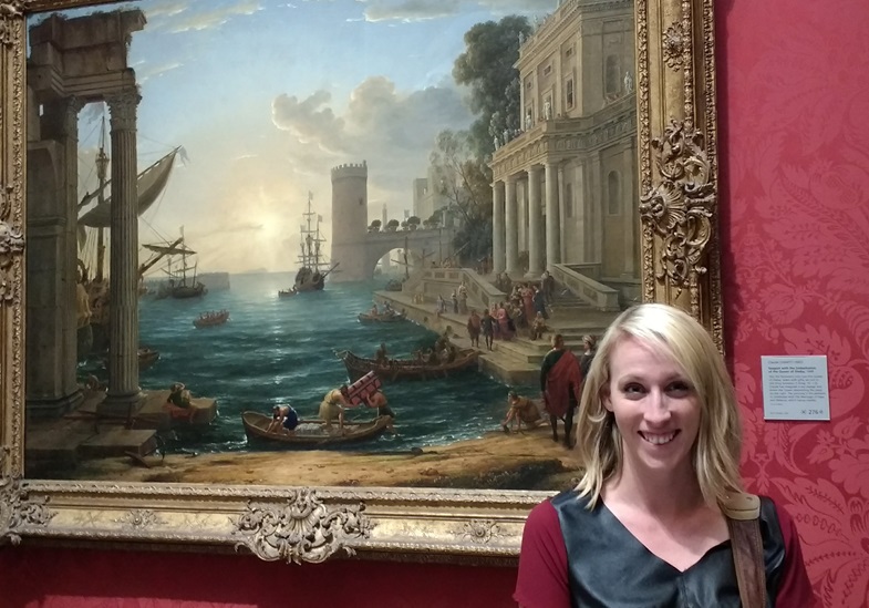 Breezy Taggart standing in front of  front of a painting titled Seaport with the Embarkation of the Queen of Sheba - oil painting by Claude Lorrain