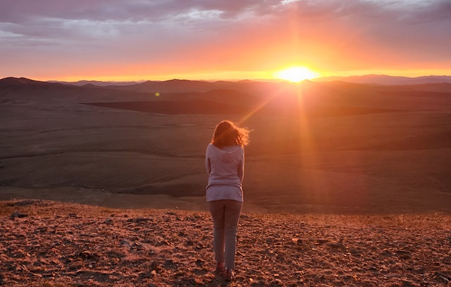 Hallie Cozzens standing in front of a sunset on a rocky landscape.