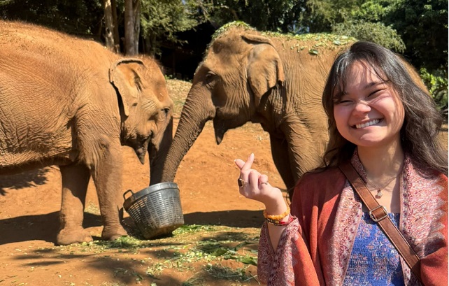 Jasmin Mahoney standing in front of two elephants with their trunks in a bucket.