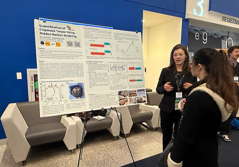 Samantha Killmer standing in front of a white poster with graphics talking to another person.