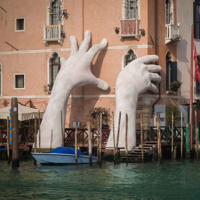 A sculpture of hands grabbing the side of a building in Venice