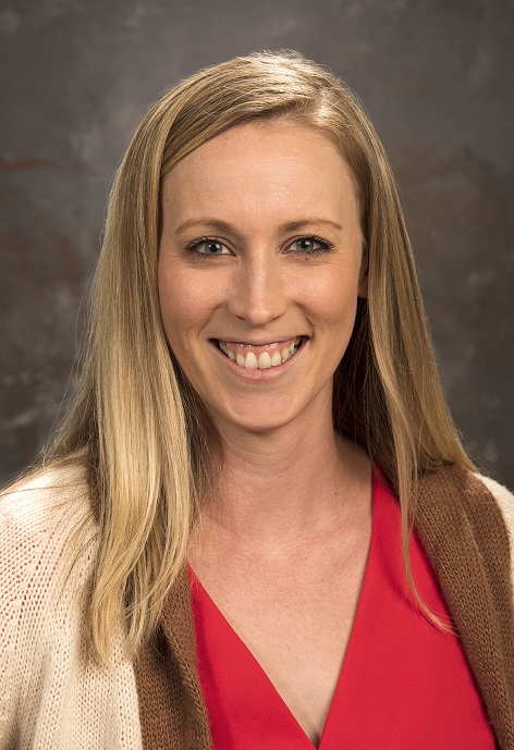 Breezy Taggart wearing a red shirt and brown sweater in front of a gray background