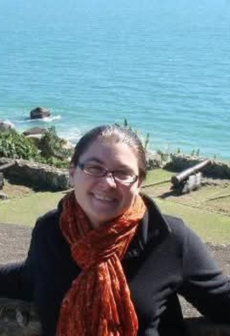 Cass Tolman wearing a black shirt with orange scarf in front of a natural landscape.