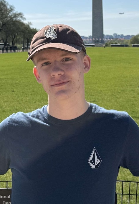 Cody Anderl wearing a brown hat and blue shirt in front of the Washington Monument.