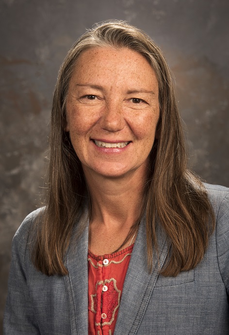 Joslyn Cassady wearing an orange shirt with a gray blazer in front of a gray background.