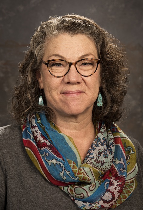 Jeanette Lamb wearing a gray shirt and patterned scarf in front of a gray background.