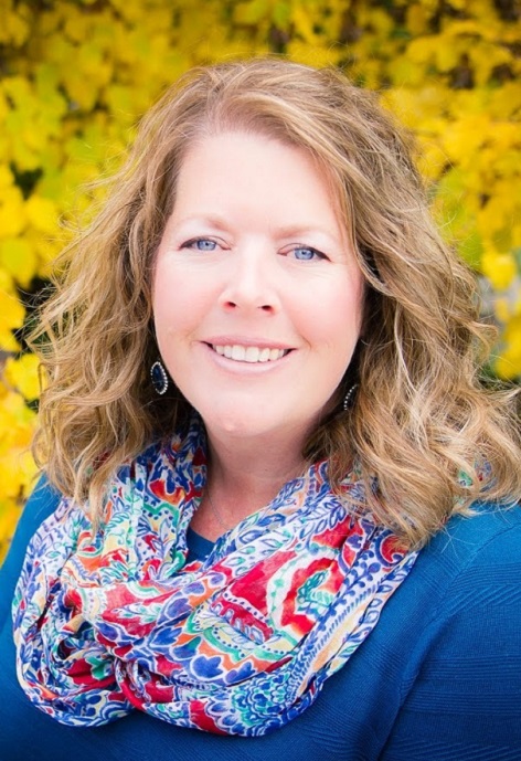 Laura Olson wearing a patterned scarf with blue shirt in front of a yellow foliage.