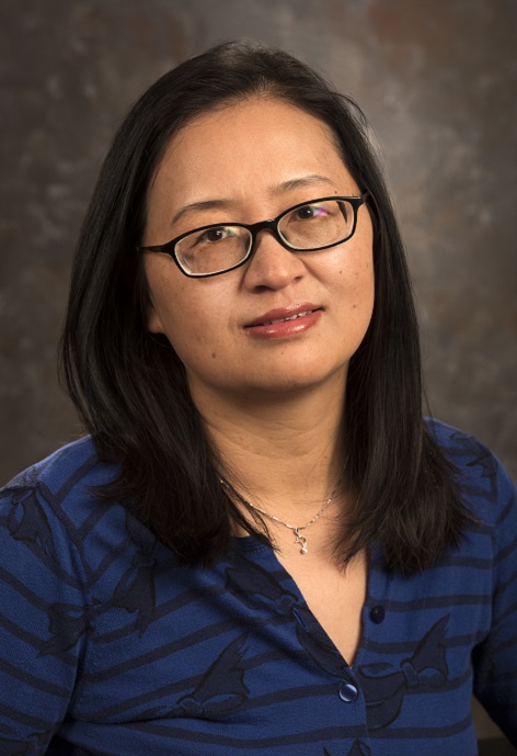 Li Teng wearing a blue and black striped shirt in front of a gray background.