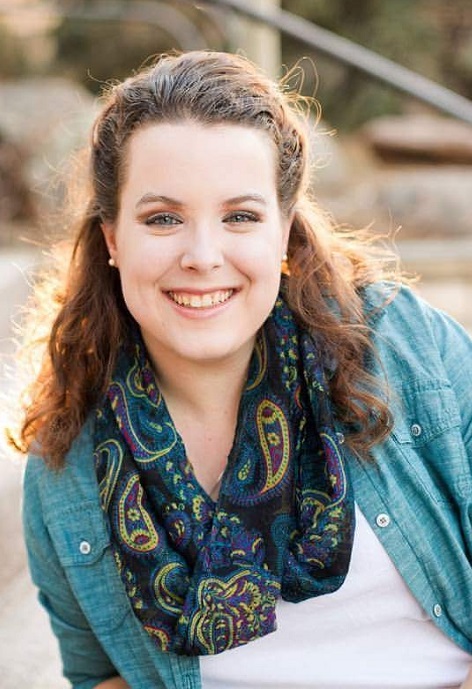 Mandie Reish wearing a blue shirt, patterned scarf in front of a blurred natural backdrop/