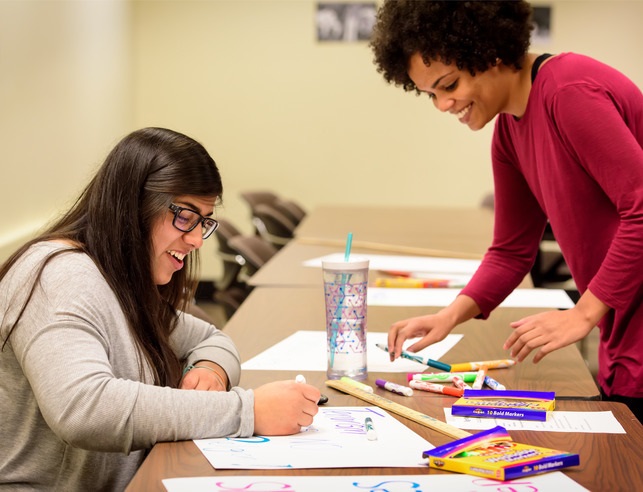 Two people collaborate on art projects at a table, surrounded by various art supplies and materials.