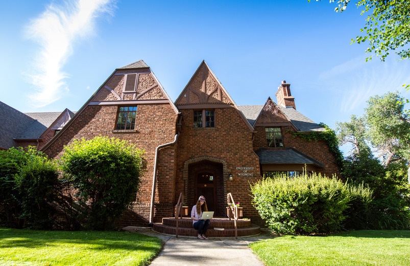 Student sitting on the front steps of a brick, historic house.