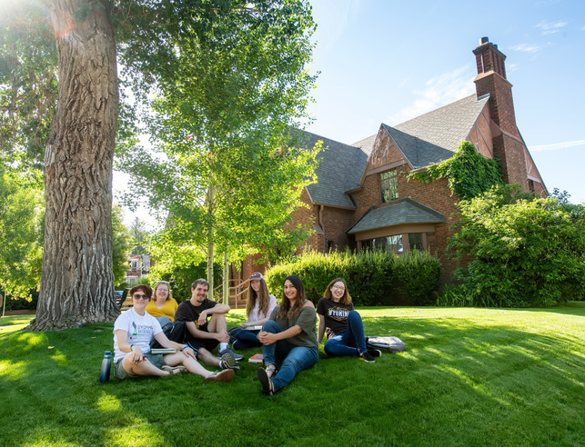 A group of students sits together on a green lawn in front of a UW building.