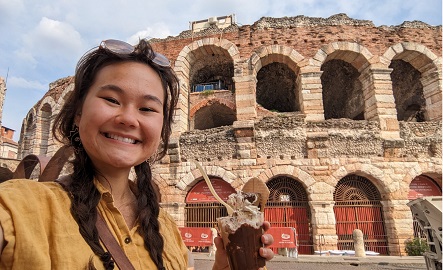 Student holding a gelato in front of a roman architectural ruin.