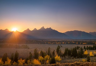 The sun rising over a yellow, orange, blue, and purple landscape.