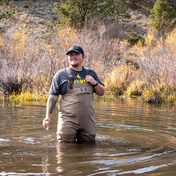Student doing field work in a river wearing gaters.