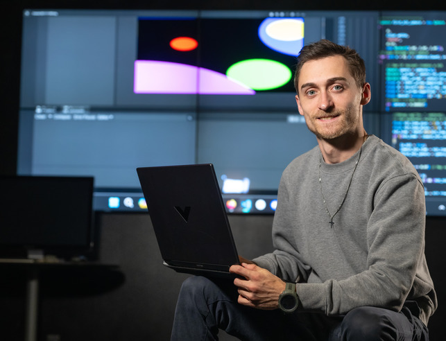 Student sitting with a laptop with screen in the background.