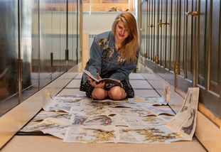 A person kneeling on the ground with many loose papers in front of them.