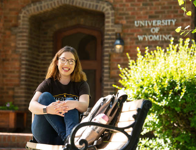 A student smiles while sitting on a bench in front of a UW building.