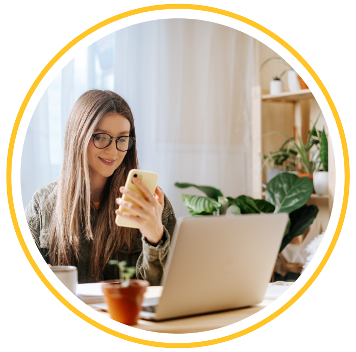 A woman is looking at her mobile phone while working at her desk.
