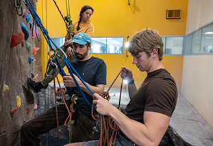 Three individuals getting ready to climb a rock wall