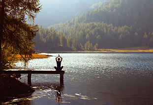 Individual meditating next to a mountain lake.