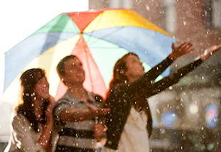 Three people under a colorful umbrella in the rain.