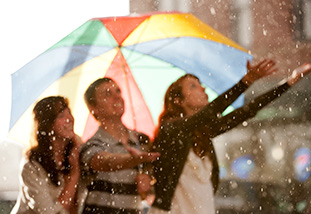 Three people in the rain with a colorful umbrella