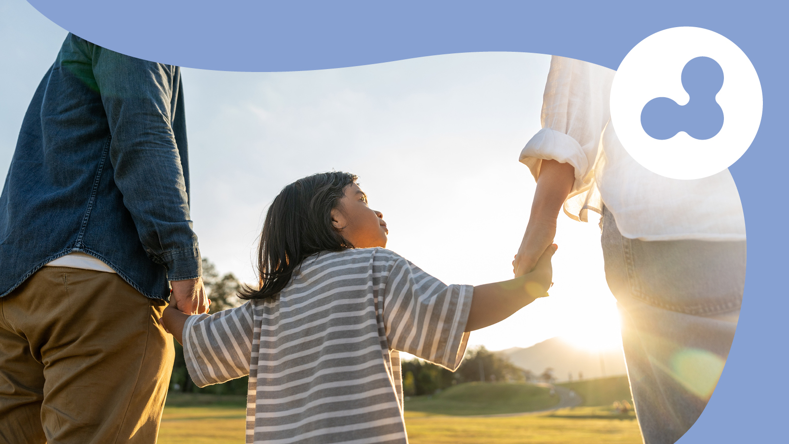 A mom and dad holding a little girl's hands as they walk in a field at sunset.