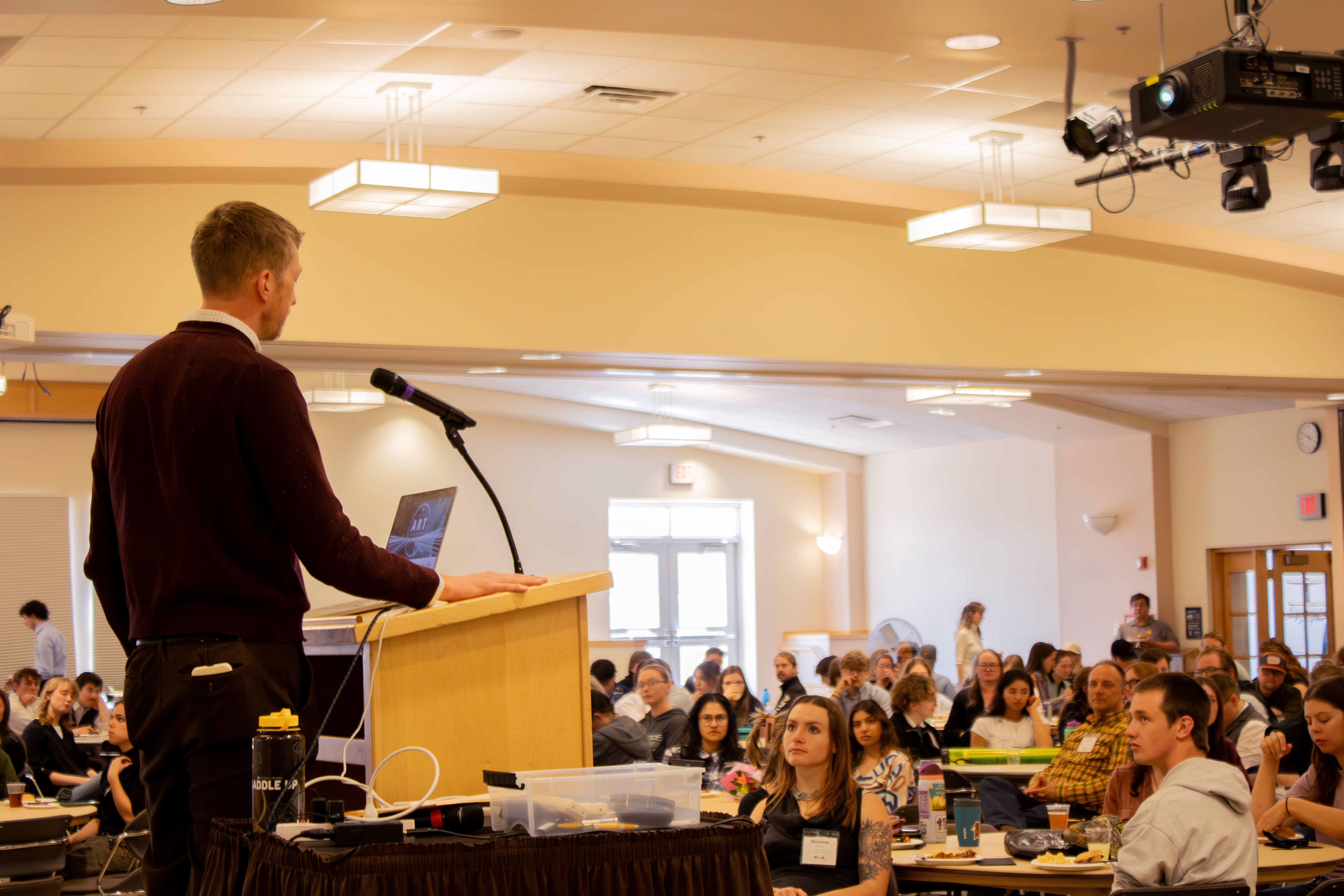 man stands in front of podium speaking to room full of people