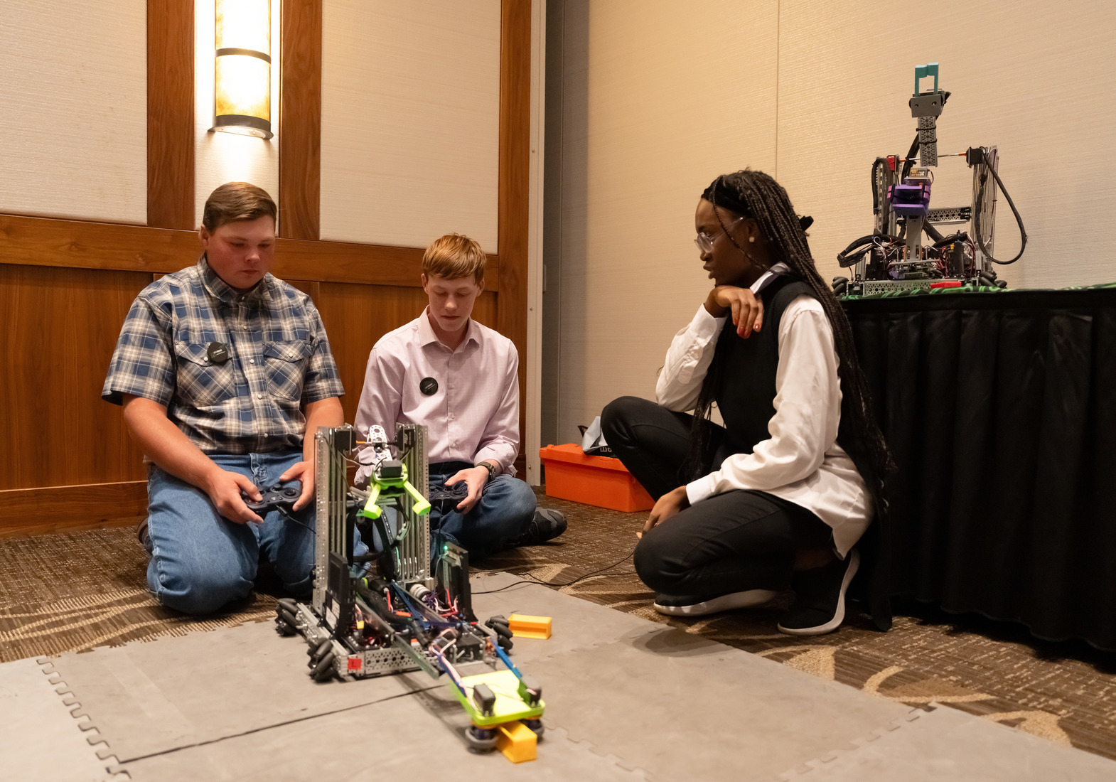 three individuals sit on floor constructing a robot