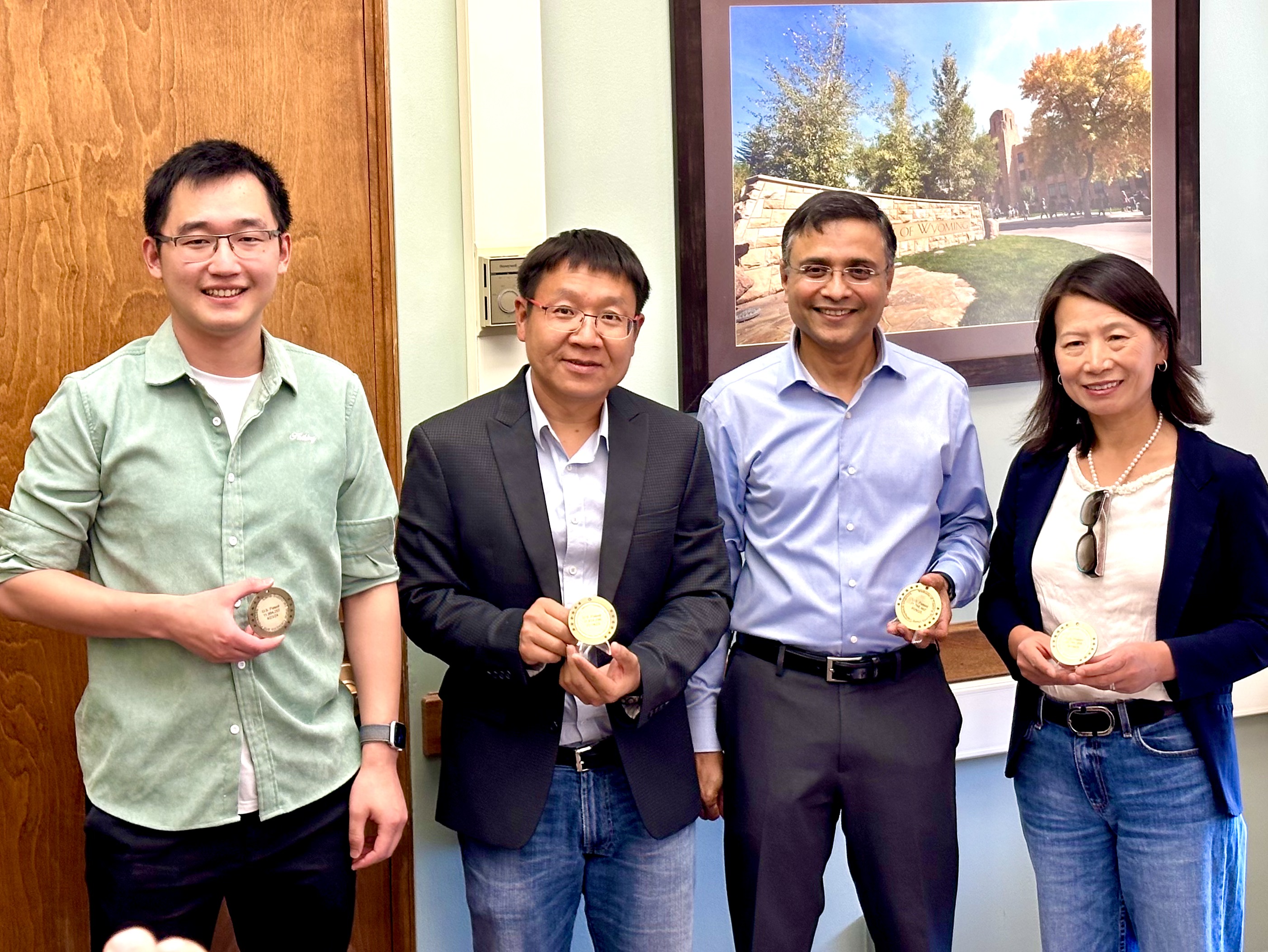 four people stand smiling holding patent medallions
